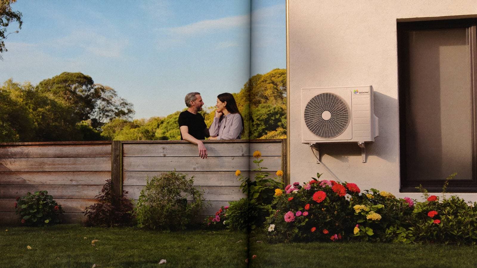 Twee buren praten ontspannen over de schutting met een nette airco-buitenunit aan de gevel