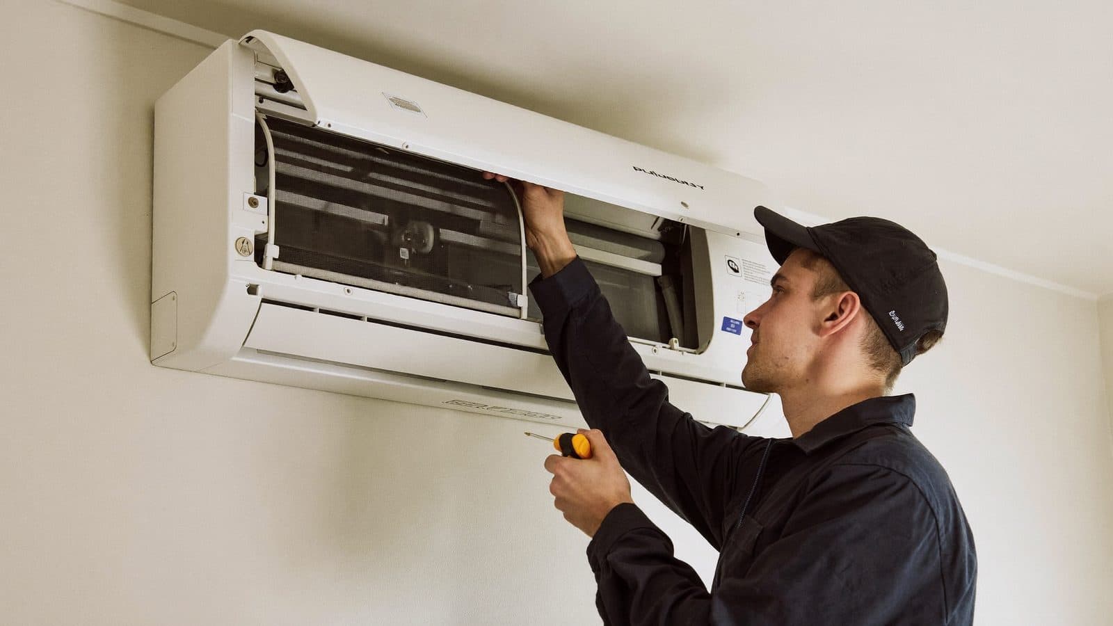 Monteur repareert een geopende binnenunit van een split-airco aan de wand