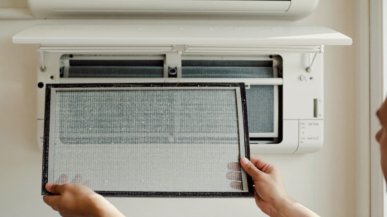 Monteur haalt een stoffige filter uit de binnenunit van een airco in een Nederlandse woonkamer
