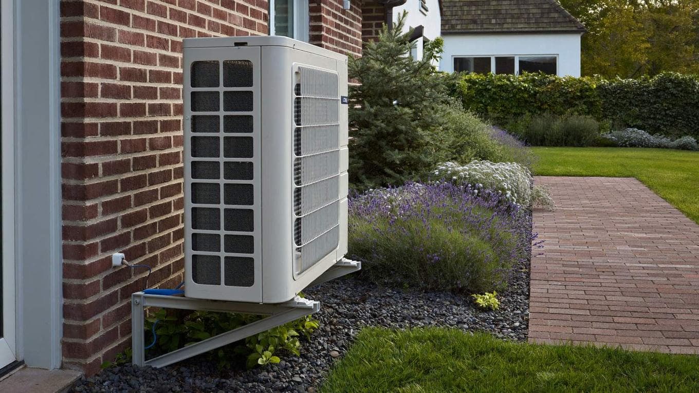 Goed onderhouden airco-buitenunit naast een Nederlands woonhuis met verzorgd tuinpad
