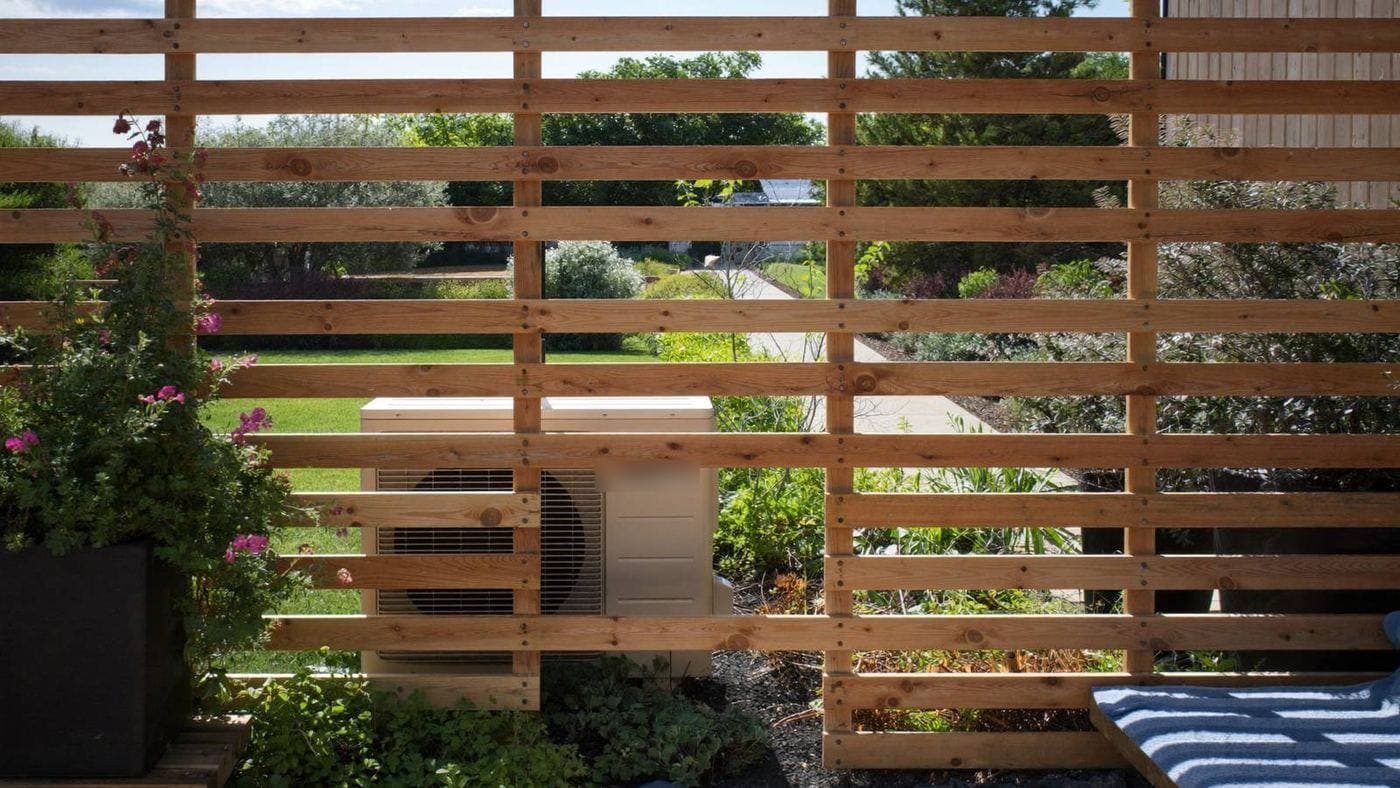 Houten lamellenomkasting rond een airco-buitenunit op een terras in een Nederlandse tuin