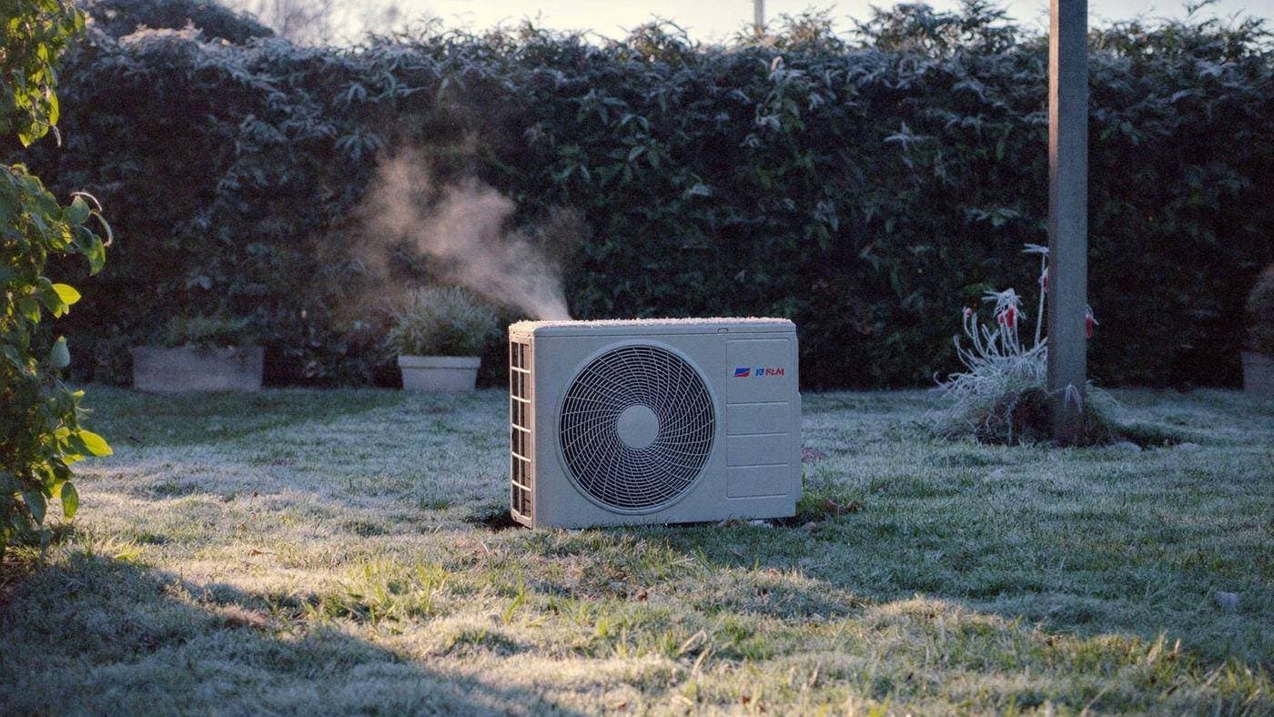 Airco-buitenunit met lichte rijp in een Nederlandse wintertuin bij zonsopkomst